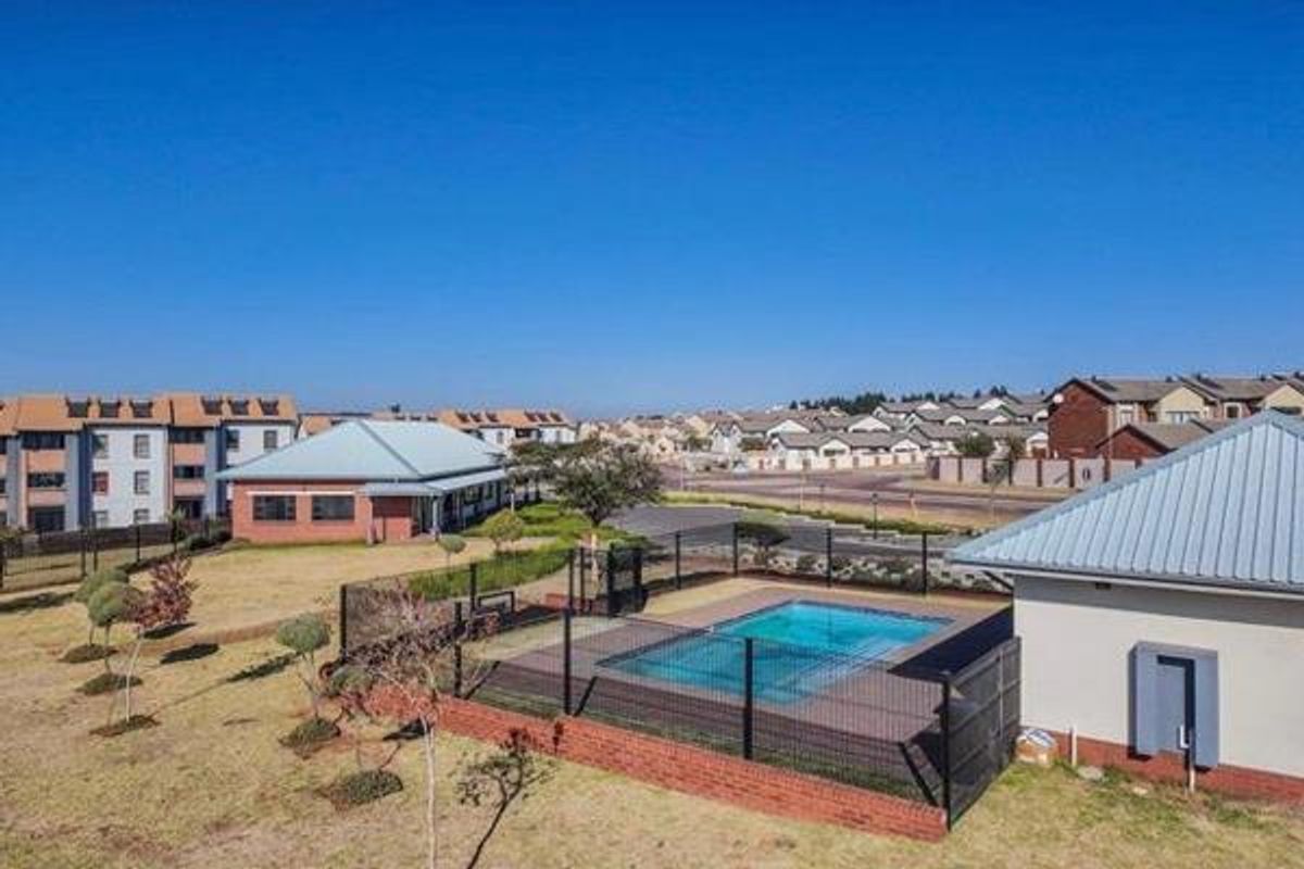 Aerial view of a residential complex featuring a communal swimming pool, landscaped grounds, and surrounding apartment buildings.