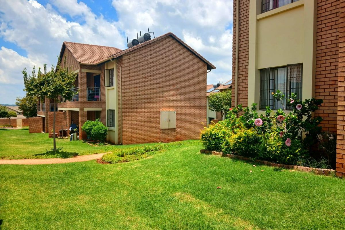 Exterior view of a multi-story apartment complex featuring face brick facades, tiled roofs, solar water heating systems, and well-maintained communal garden areas.