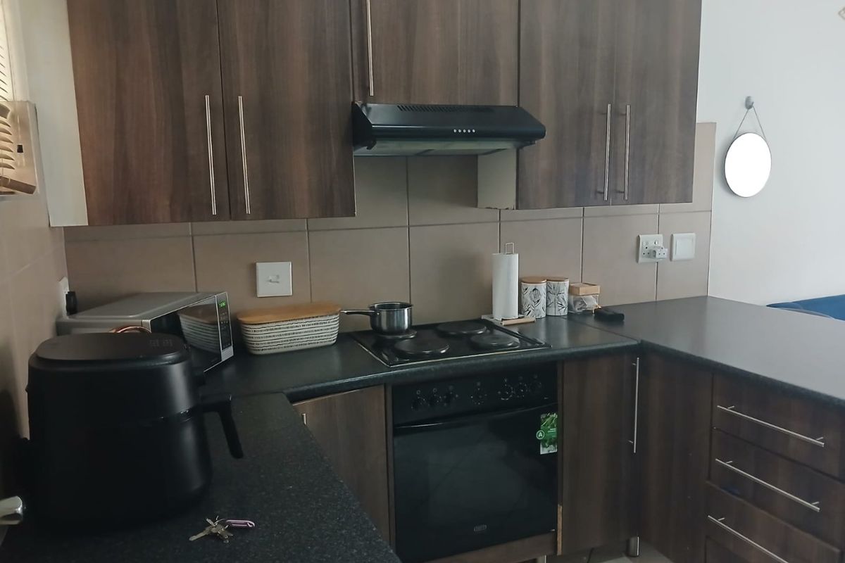 A functional kitchen featuring dark wood-look cabinetry, laminate countertops, a built-in oven, electric hob, and an extractor fan with tiled backsplash.