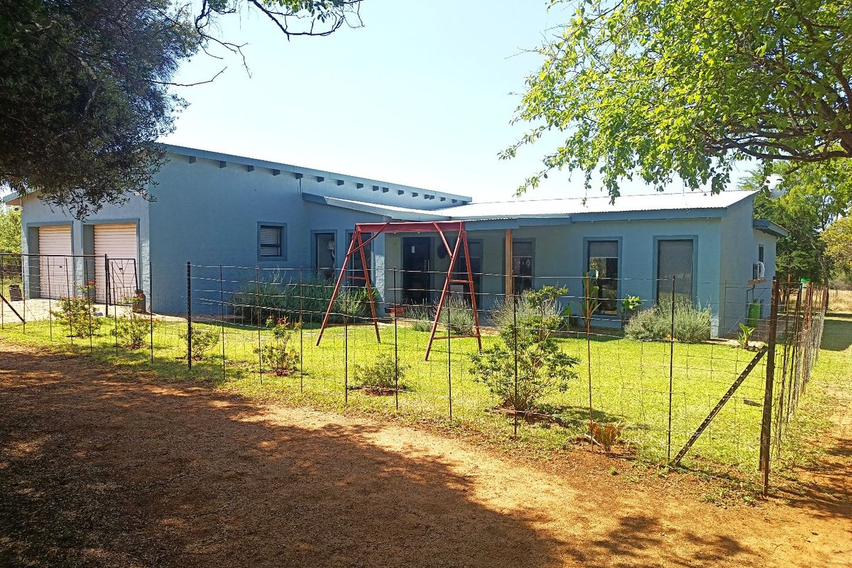 Rear view of a single-story farm house featuring a blue exterior, metal roofing, a covered patio area, and an attached double garage.