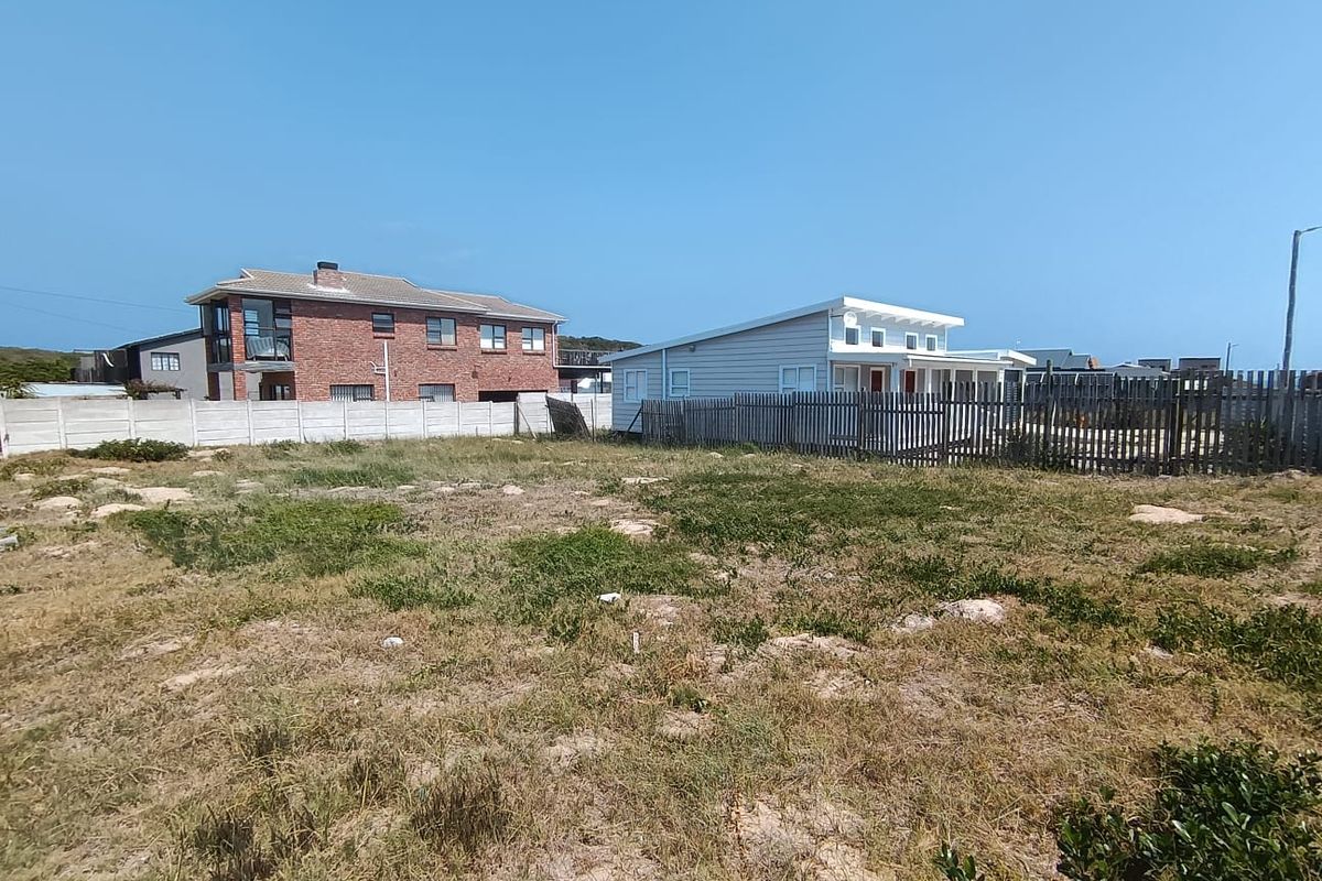 A vacant residential plot featuring natural ground cover, enclosed by a combination of precast concrete walling and timber fencing.