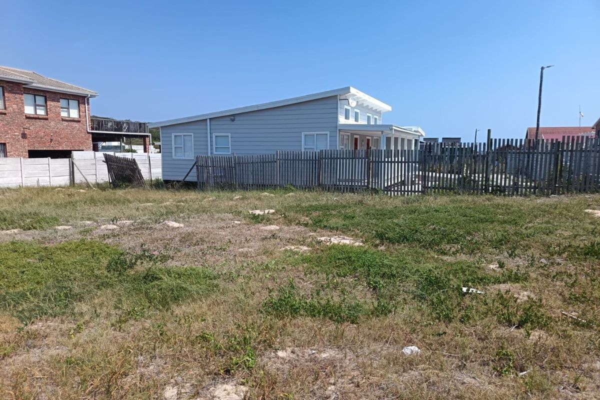 A view of a vacant residential plot featuring a timber picket fence and adjacent weatherboard dwelling.