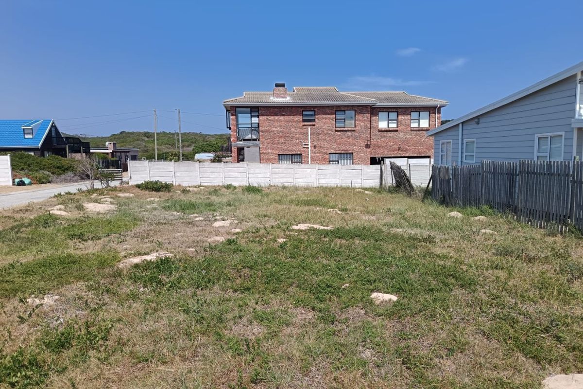 A vacant residential plot of land featuring natural grass cover, enclosed by a precast concrete boundary wall and a timber fence.