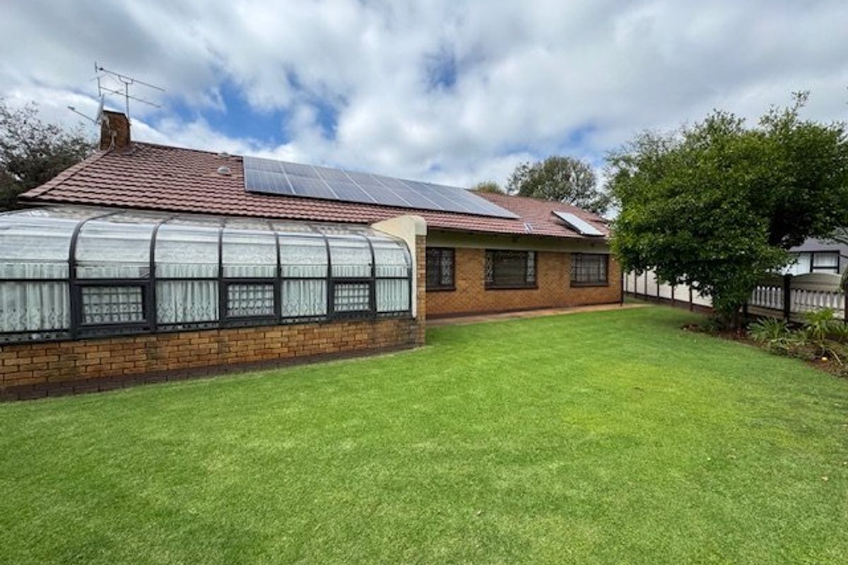 Rear view of the property featuring a brick facade, tiled roof with solar panels, and an attached sunroom overlooking a well-maintained lawn.
