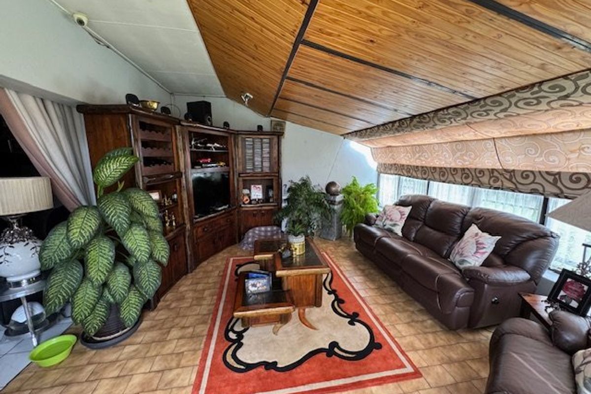 A living room featuring a distinctive timber-clad raked ceiling, ceramic floor tiles, and built-in timber cabinetry providing ample storage space.