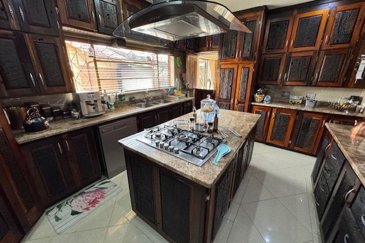 Spacious kitchen featuring dark wood cabinetry, granite countertops, a central island with a gas hob, and an overhead extractor fan.