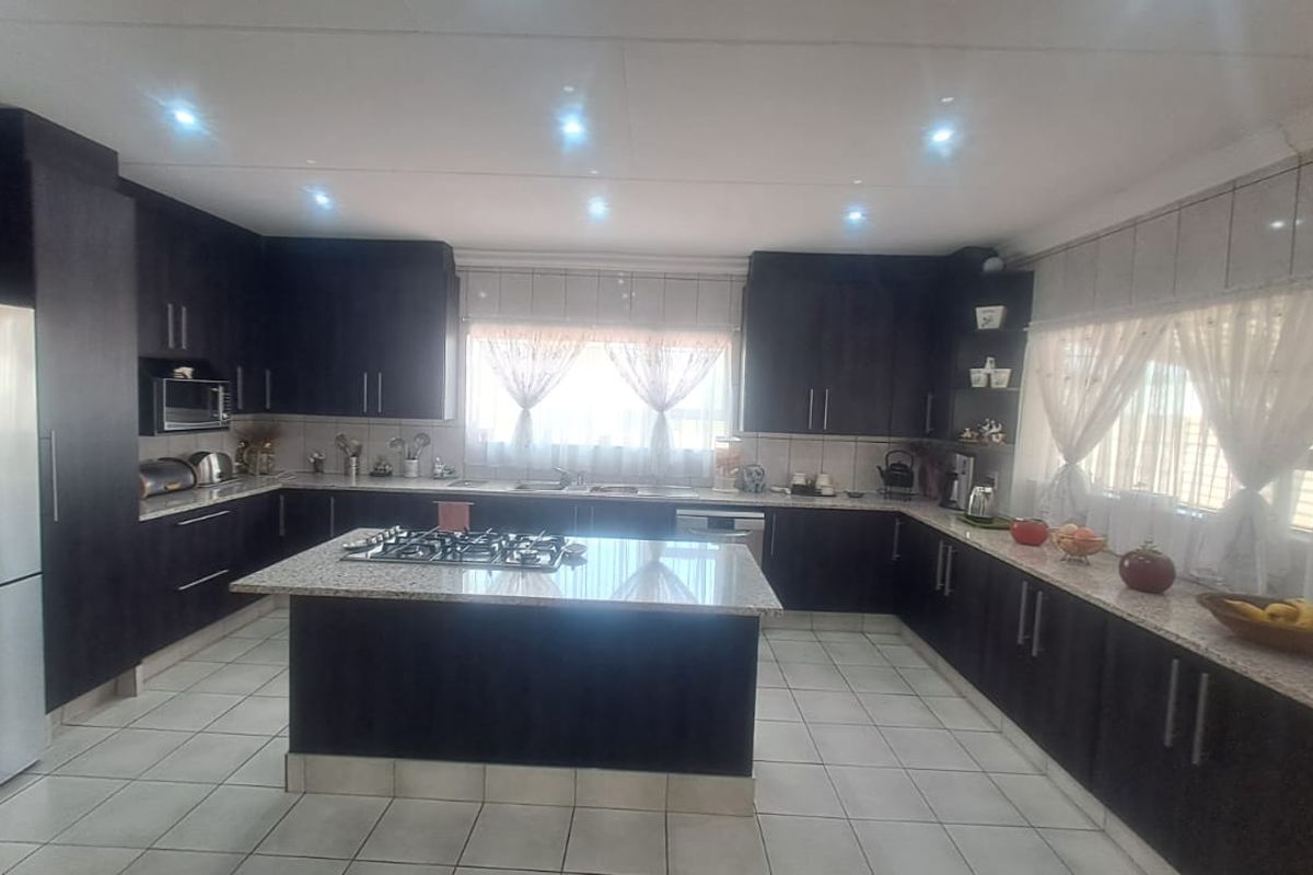 Spacious kitchen featuring dark wood cabinetry, granite countertops, a central island with a gas hob, and tiled flooring throughout.