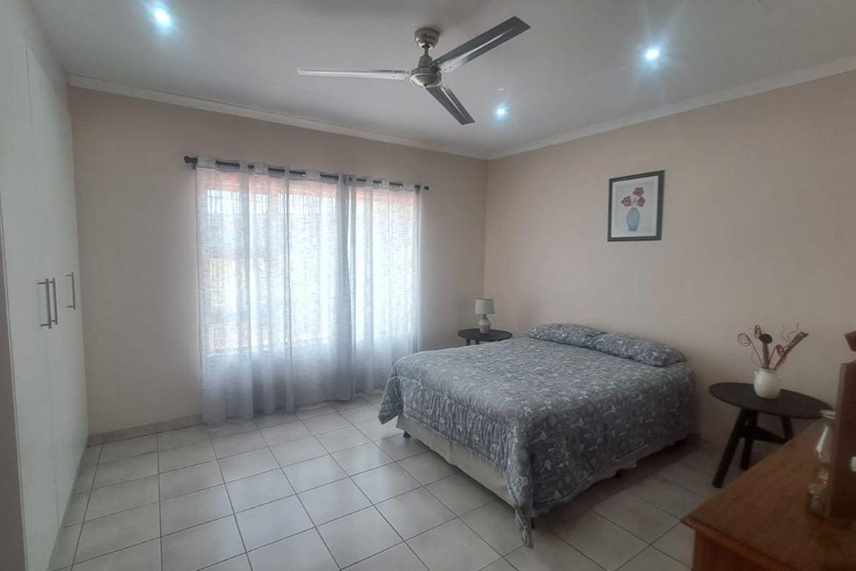 A well-maintained bedroom featuring tiled flooring, built-in cupboards, and a ceiling fan, offering a clean and functional living space.