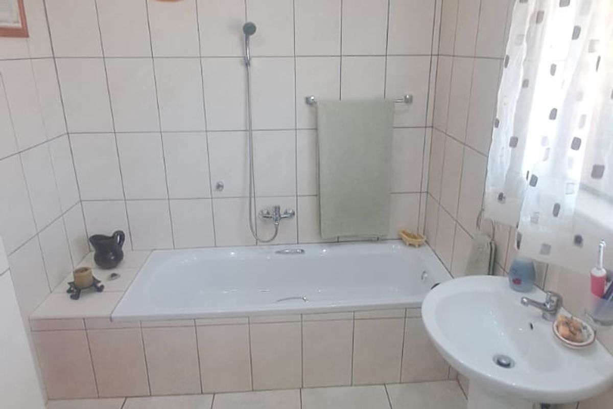 A functional bathroom featuring full-height wall tiling, a built-in bathtub with shower mixer, and a classic pedestal washbasin.