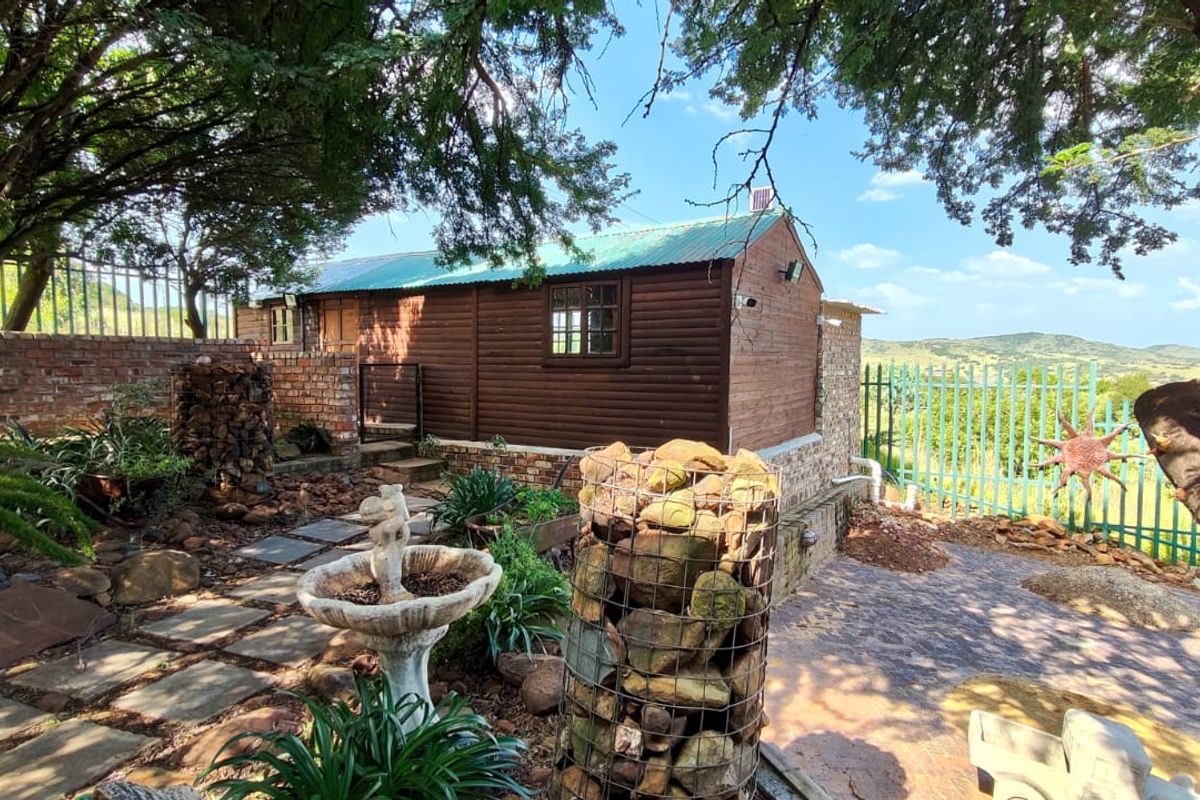 A rustic timber-clad structure set within a landscaped garden featuring stone gabion walls, brick retaining elements, and a paved outdoor area with scenic views.