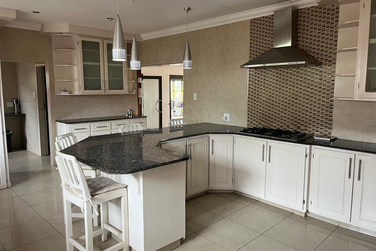 Spacious kitchen featuring granite countertops, white cabinetry, a gas hob with stainless steel extractor, and a breakfast bar island.