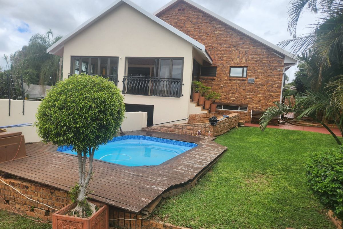 Rear exterior view featuring a swimming pool with timber decking, a landscaped garden, and a multi-level brick and rendered facade with a balcony.
