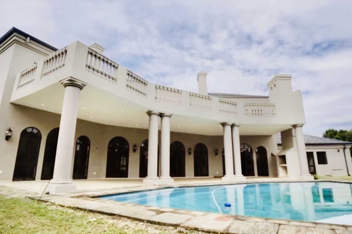 Spacious rear exterior featuring a large swimming pool, expansive covered patio with classic columns, and elegant arched doorways leading into the home.