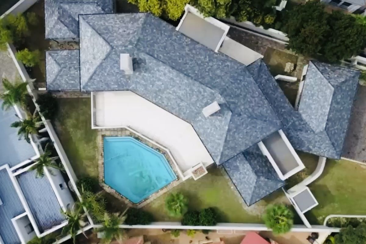 Aerial view of a residential property featuring a tiled roof, a swimming pool, and a paved patio area within a walled garden.