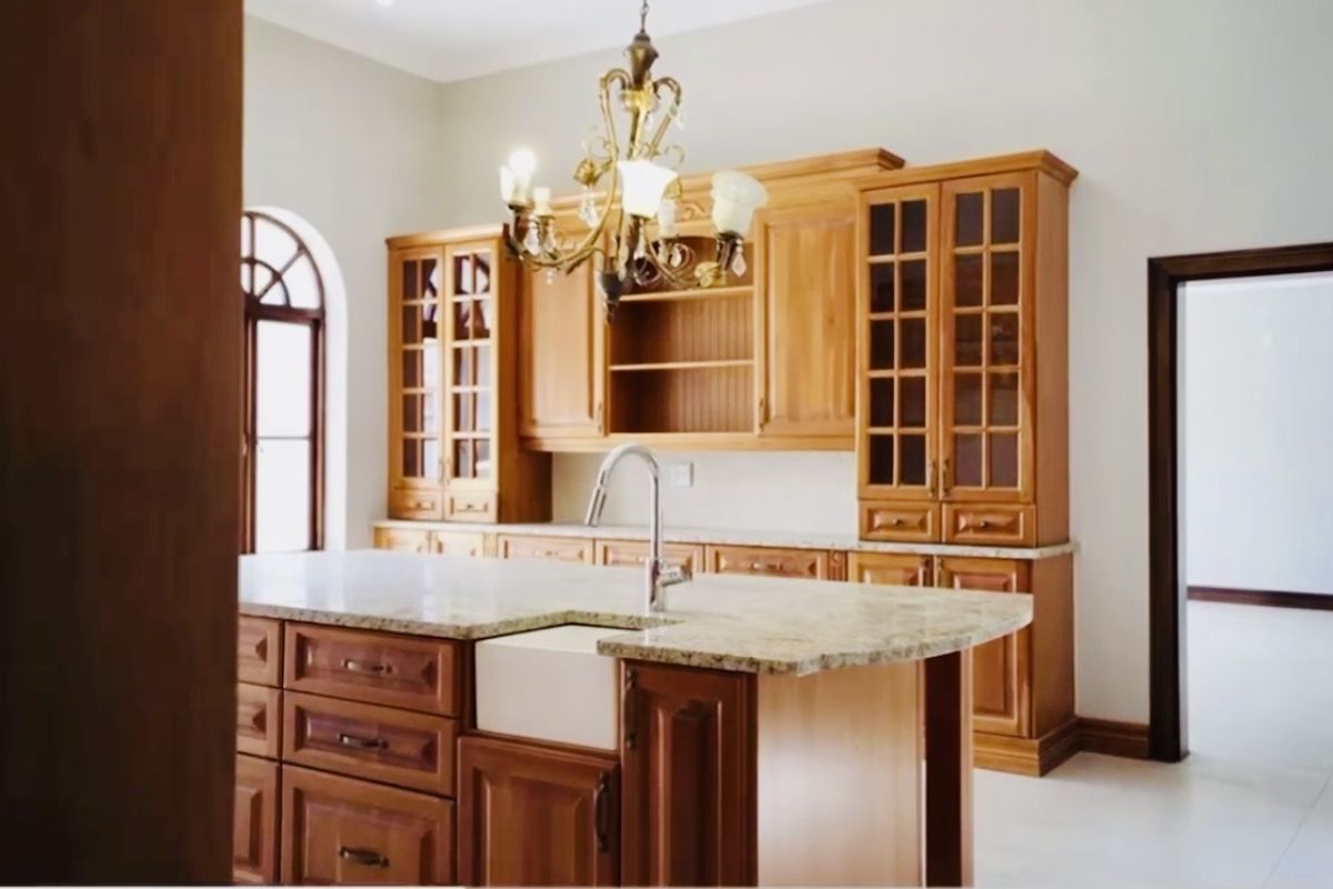 Spacious kitchen featuring warm wooden cabinetry, granite countertops, a central island with an apron-front sink, and an elegant arched window.