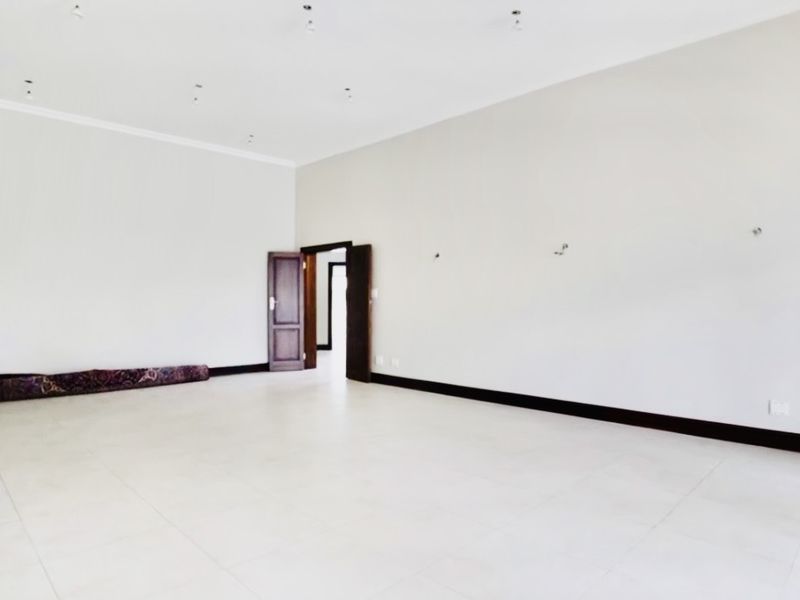 A spacious, empty living area featuring neutral tiled flooring, coved ceilings, and recessed downlighting, providing a blank canvas for interior design.