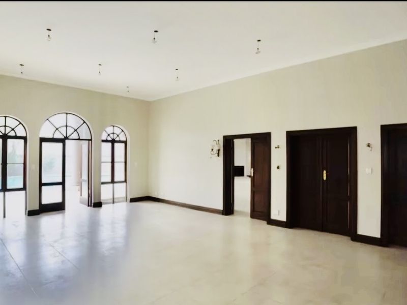 Spacious, light-filled living area featuring elegant arched windows, tiled flooring, and dark wood double doors leading to other parts of the home.
