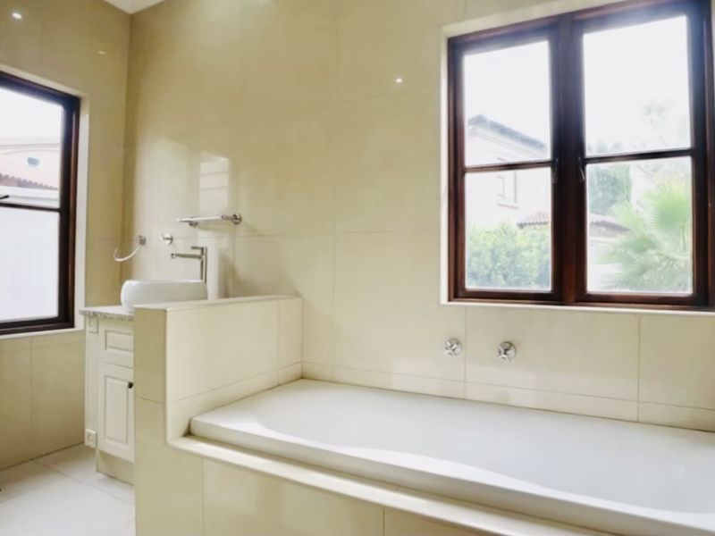 A bright, neutral-toned bathroom featuring a built-in bathtub, a vanity with a vessel sink, and a separate glass-enclosed shower area.