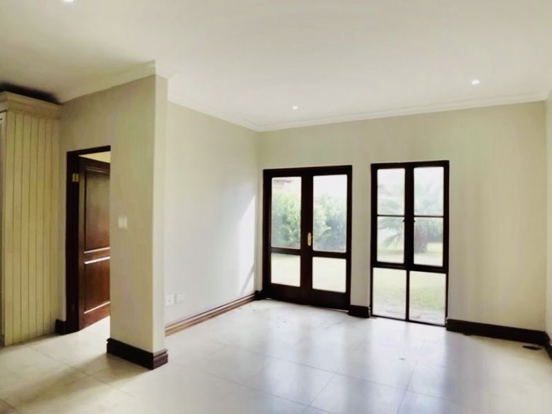 A bright, empty bedroom featuring tiled flooring, built-in cabinetry, and timber-framed glass doors providing direct access to the garden.