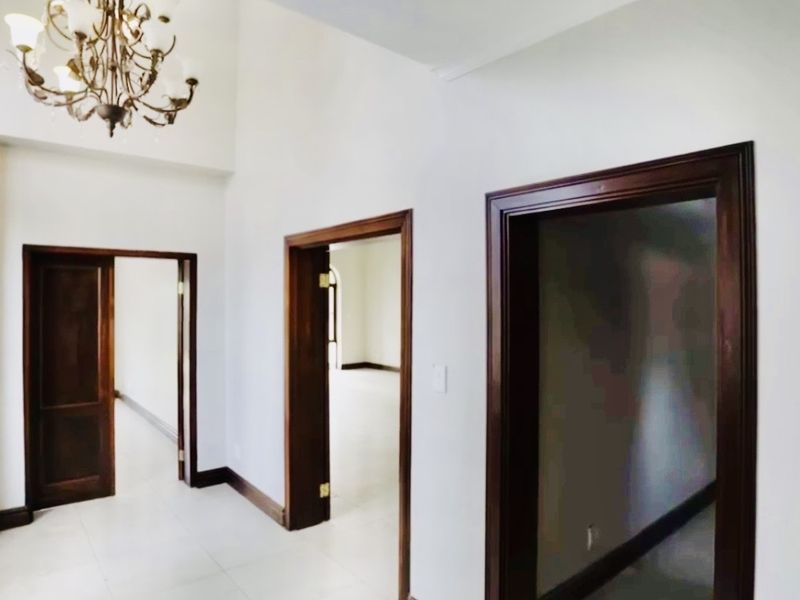 A spacious, empty hallway featuring high ceilings, a decorative chandelier, and dark wood door frames leading into adjacent rooms.