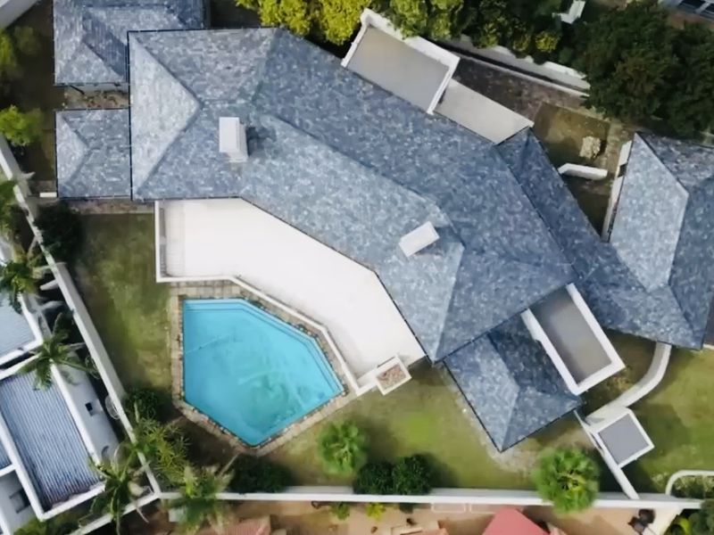 Aerial view of a residential property featuring a tiled roof, a swimming pool, and a paved patio area within a walled garden.