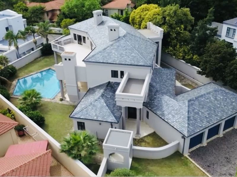 Aerial view of a large residential property featuring a slate roof, private swimming pool, multi-car garage, and landscaped garden areas.