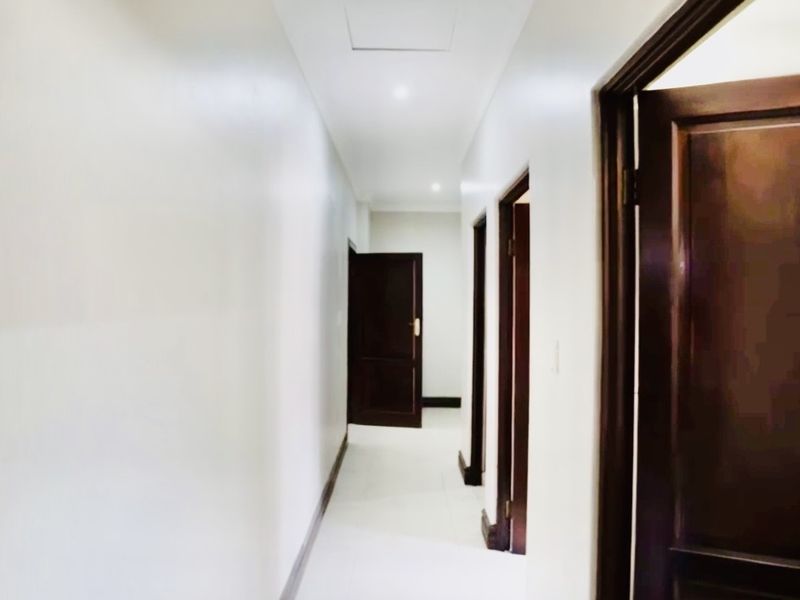 A clean, well-lit interior hallway featuring neutral walls, tiled flooring, and dark timber doors leading to adjacent rooms.