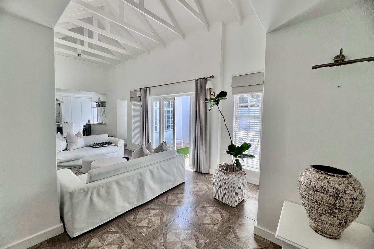 Bright and airy living room featuring a high vaulted ceiling with exposed rafters, elegant patterned tile flooring, and direct access to an outdoor patio area.