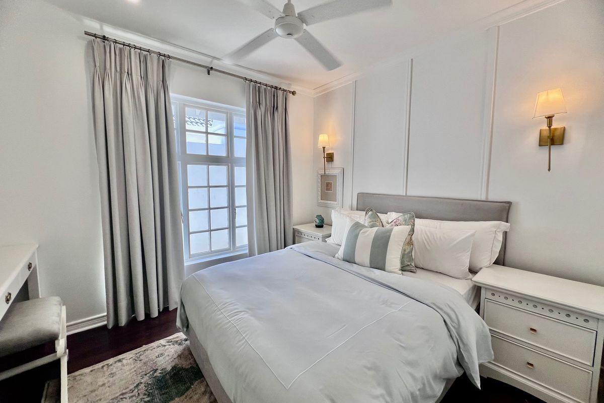 A well-maintained bedroom featuring elegant wall paneling, recessed lighting, a ceiling fan, and warm wall sconces, creating a bright and inviting atmosphere.