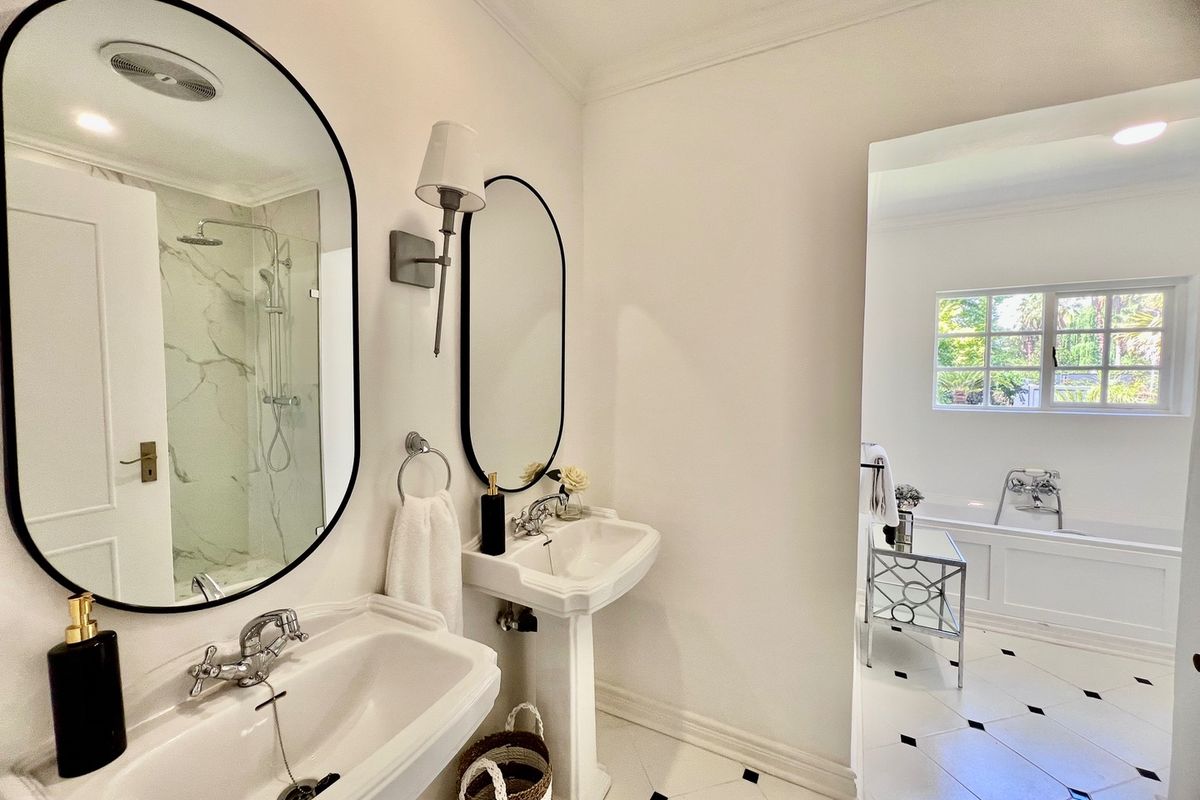 Elegant bathroom featuring dual pedestal sinks, a glass-enclosed shower, and a separate built-in bathtub with classic black and white tiled flooring.