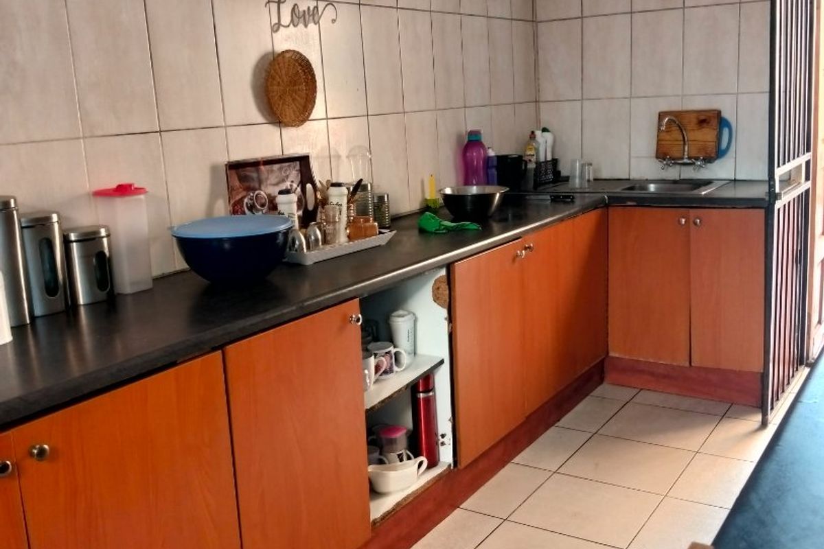 A functional kitchen featuring laminate cabinetry, tiled walls and flooring, and a stainless steel sink, currently showing signs of wear and maintenance needs.