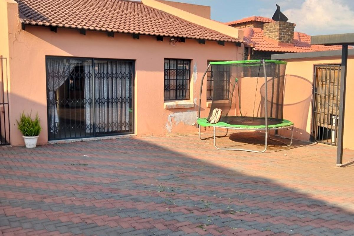 Rear exterior view featuring a paved patio area, tiled roof, and security gates, with visible wear to the exterior wall plaster and paint.