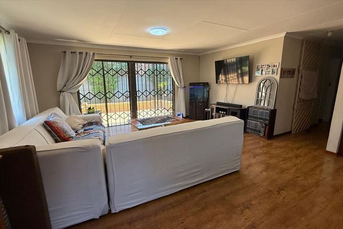 A comfortable living room featuring laminate flooring, a ceiling light, and sliding glass doors with security gates leading to an outdoor area.