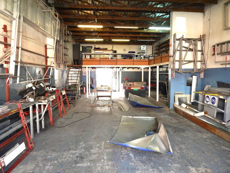 Industrial workshop space featuring a mezzanine level, exposed timber roof trusses, concrete flooring, and functional metal staircase access.