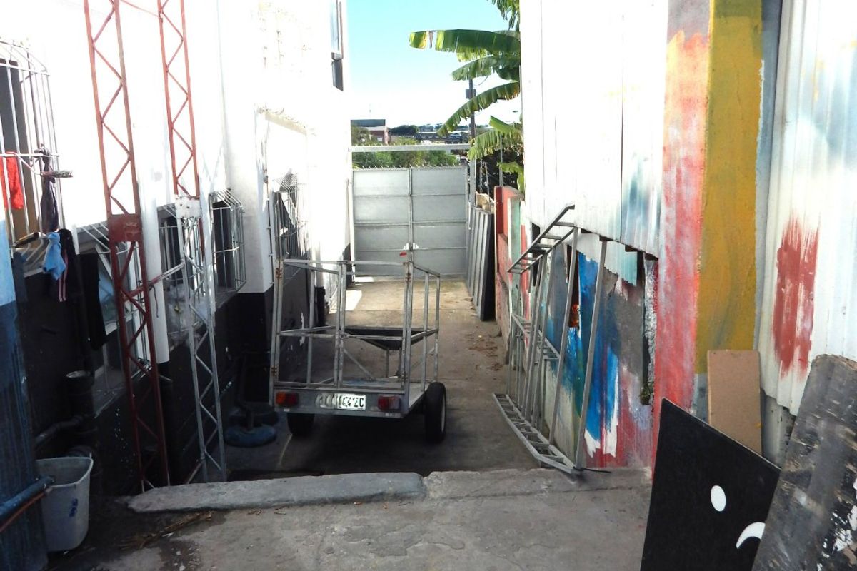 Narrow rear exterior access area featuring concrete paving, security gates, and industrial wall finishes.