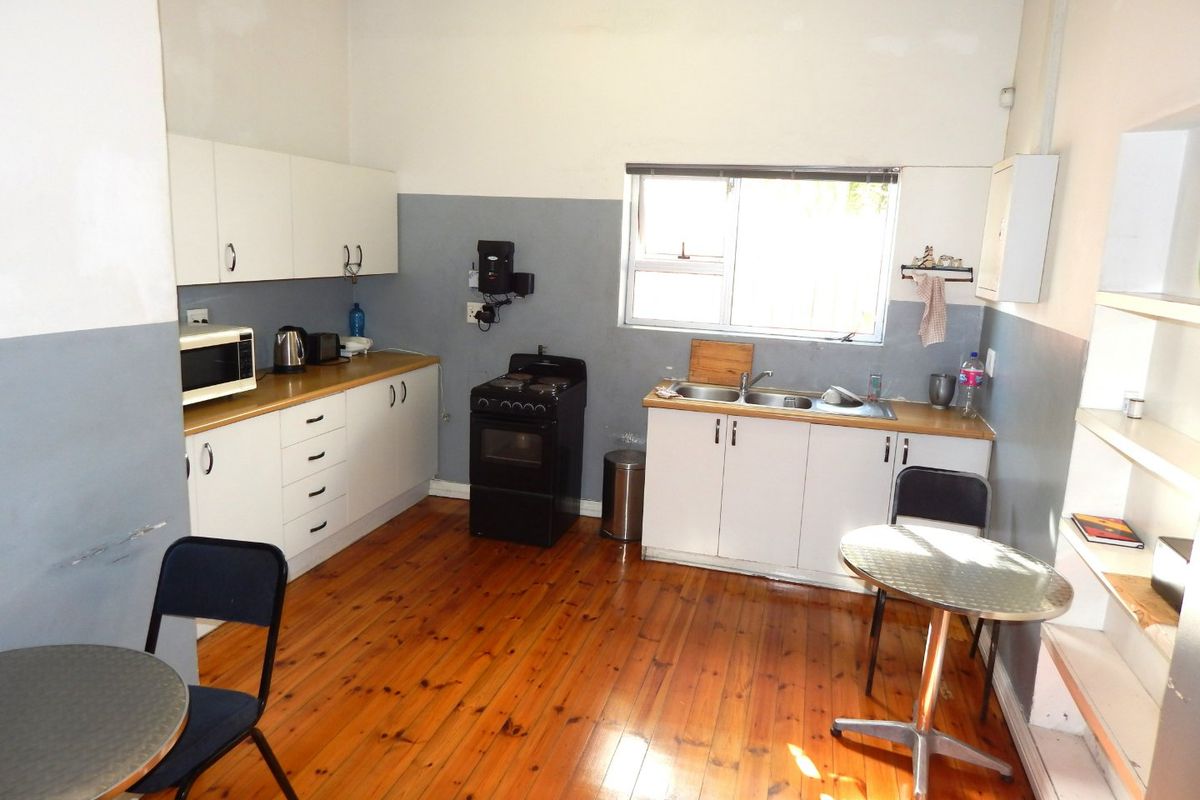 A functional kitchen area featuring timber flooring, white cabinetry, a double sink, and a freestanding stove, requiring cosmetic updates to the wall finishes.