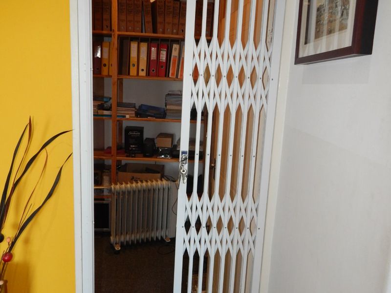 A utility storage area secured by a white metal concertina security gate, featuring built-in shelving for organized storage.