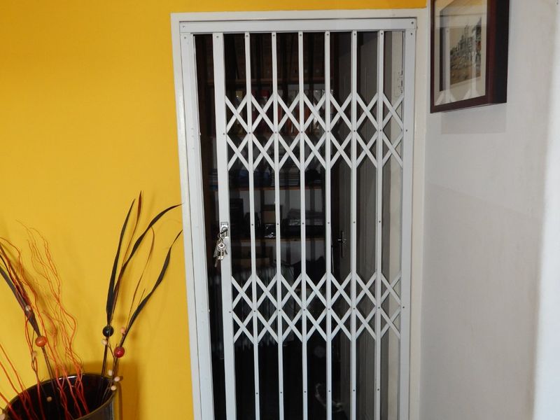 A hallway interior featuring a white metal security gate and tiled flooring, providing access to an adjacent utility or storage space.