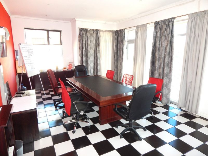 A functional office space featuring high-contrast checkered tile flooring, recessed lighting, and large windows providing ample natural light.