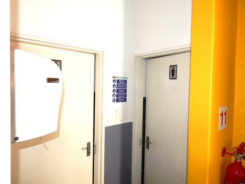 A functional industrial restroom entrance area featuring standard doors, signage, and wall-mounted safety equipment including a fire extinguisher and paper towel dispenser.