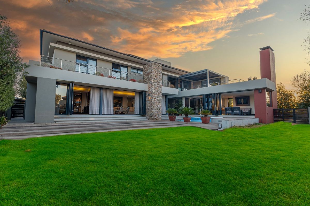 Stunning rear elevation of a modern luxury home featuring a swimming pool, expansive decking, stone accents, and seamless indoor-outdoor flow through bi-fold doors.