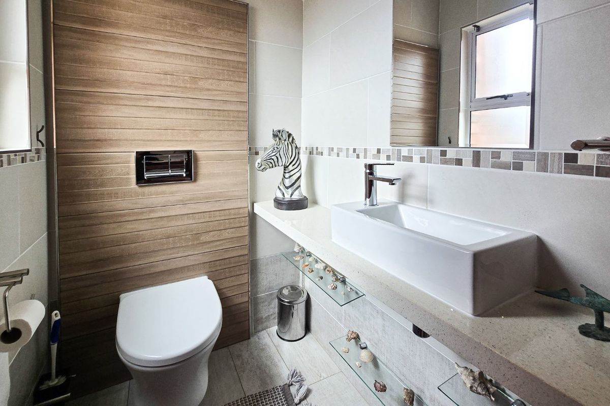 Modern bathroom featuring a wall-mounted toilet, floating vanity with a vessel sink, and contemporary tiled finishes with glass shelving.