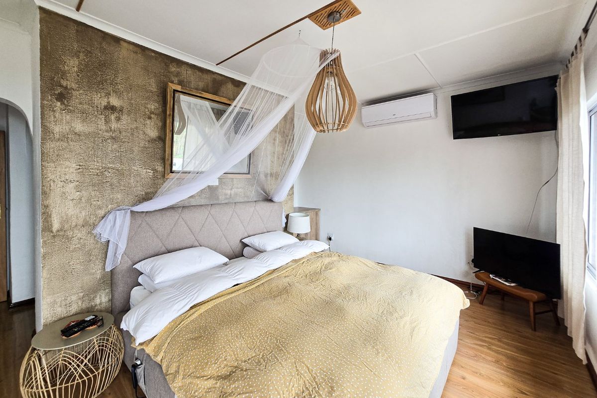 A well-maintained bedroom featuring laminate flooring, a textured feature wall, and a wall-mounted split-system air conditioner for climate control.