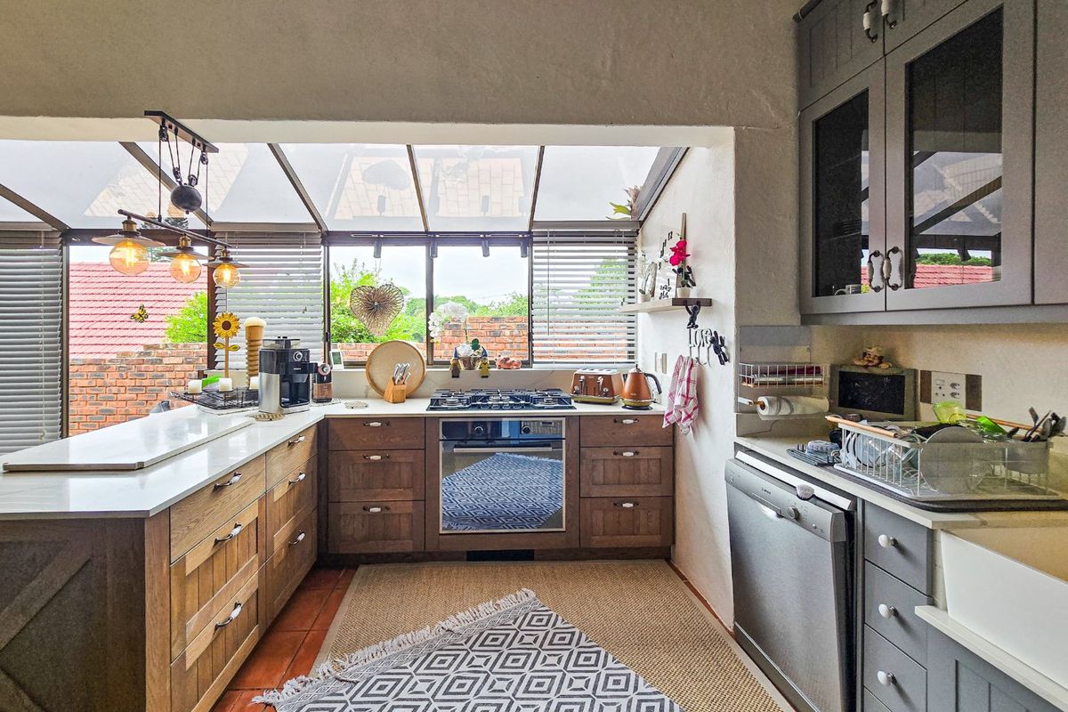 A well-appointed kitchen featuring custom cabinetry, stone countertops, a gas hob, built-in oven, and a bright conservatory-style glass roof.