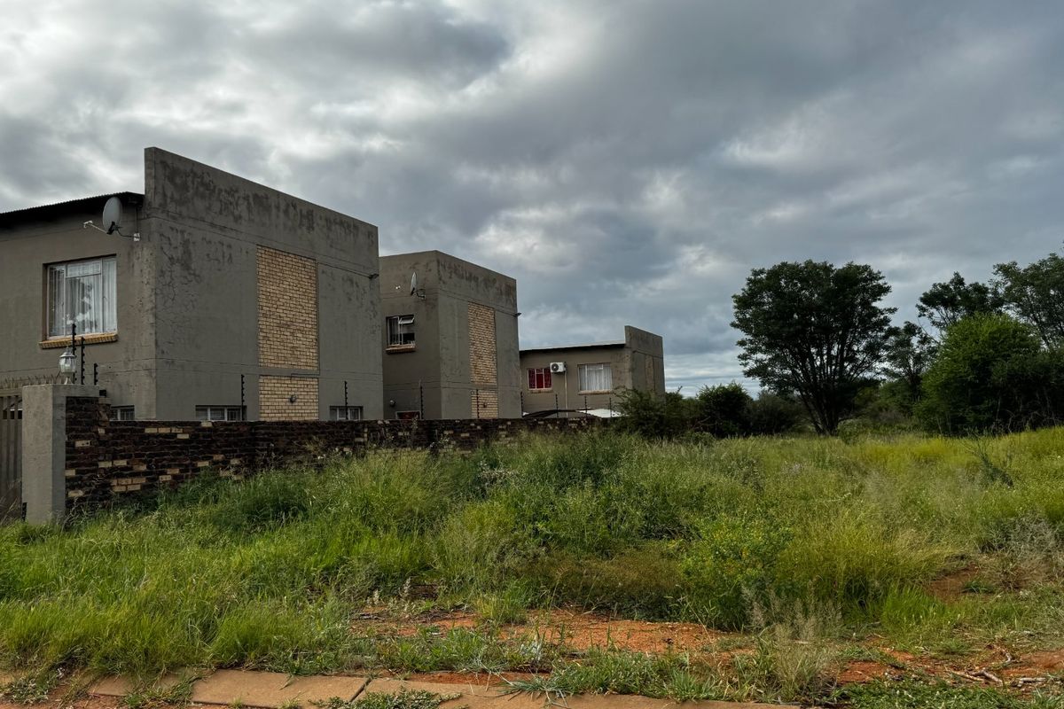 View of a residential property featuring a brick boundary wall with electric fencing, adjacent to an undeveloped plot of land.