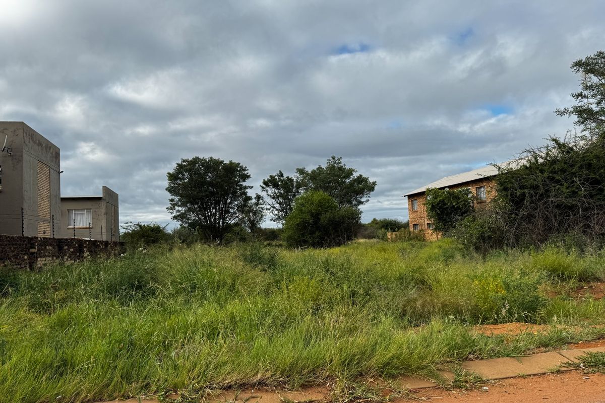 A vacant residential plot featuring overgrown grass, boundary walls, and existing electric fencing, situated in a developed neighborhood setting.