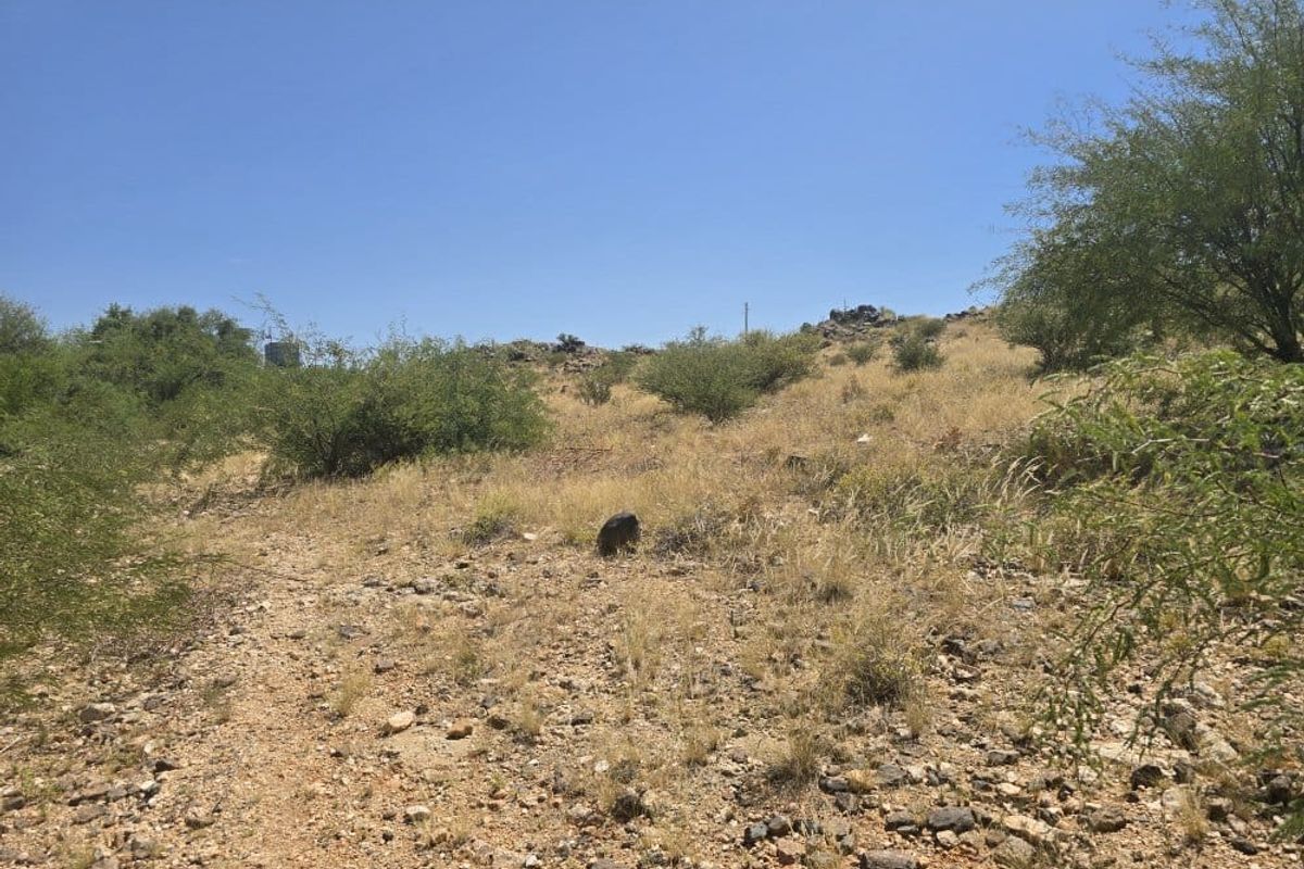 A view of the vacant residential land featuring natural rocky terrain and native vegetation under a clear blue sky.