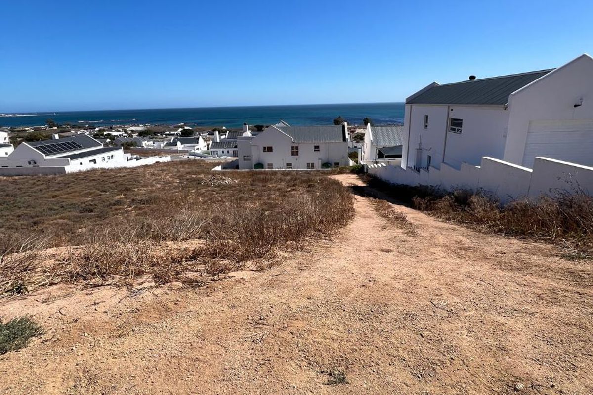 A vacant residential plot featuring a gentle slope, direct street access, and scenic coastal views in a developed neighborhood.