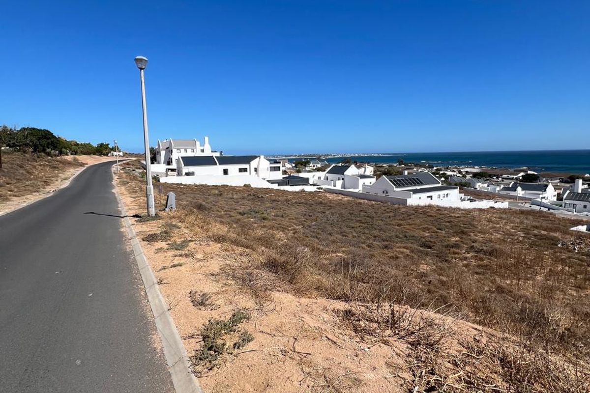 A street-level view of a residential area featuring an asphalt road, concrete curbing, and a clear view of the coastal landscape.