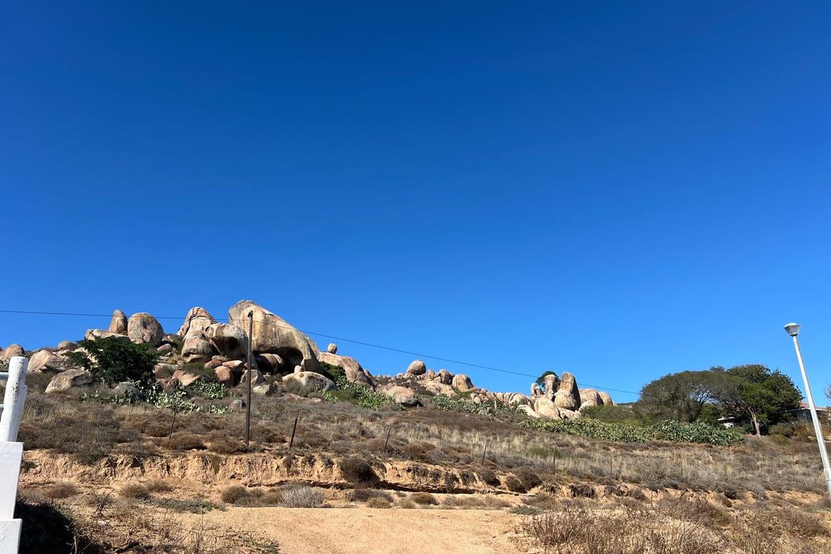 A view of the vacant residential land featuring natural rocky terrain, native vegetation, and existing utility infrastructure under a clear blue sky.